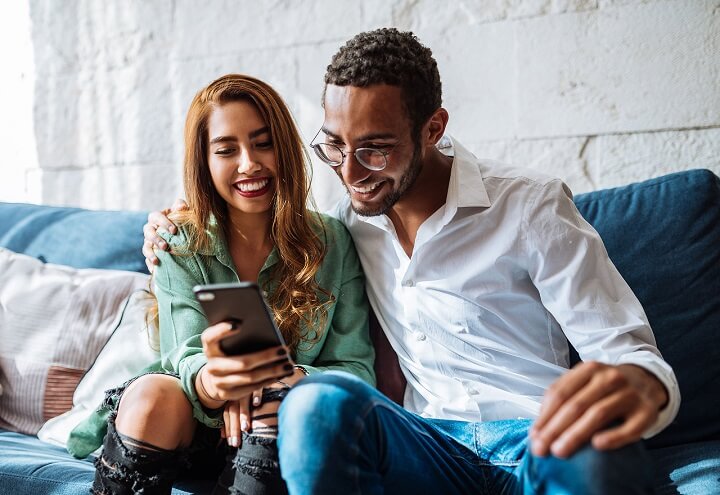 Couple sitting on couch looking at mobile device.