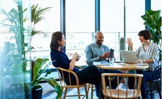 Coworkers sitting at a table talking with laptops open.