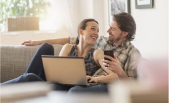 Couple sitting on a couch together while using electronic devices.