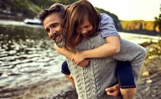 Father and daughter walking outside near lake.