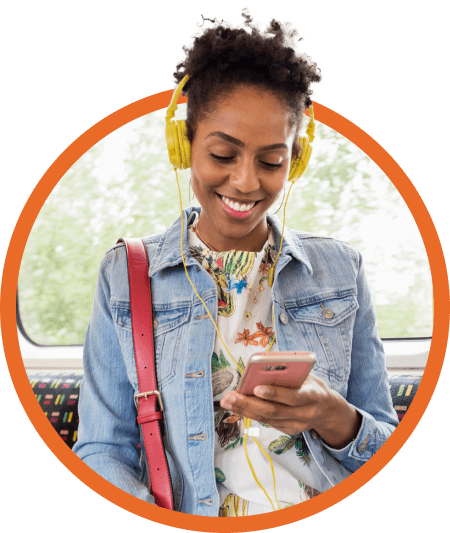 Young woman wearing jean jacket and headphones smiles while using her mobile device.