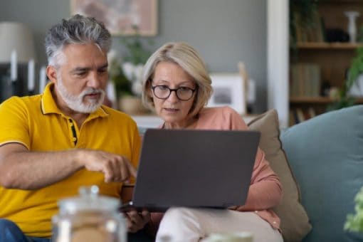 A middle-aged couple on a sofa compare credit card reward offers on their laptop.