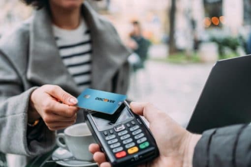 A person making a contactless credit card payment at a sidewalk café. 