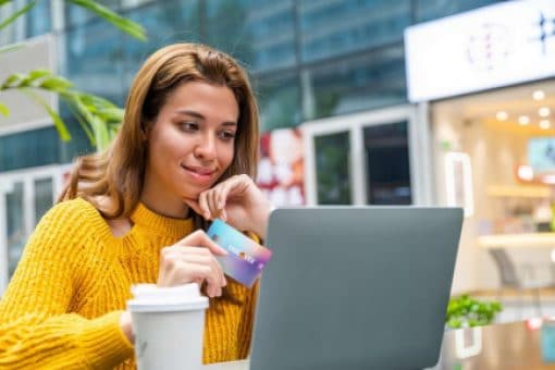 Young woman uses her Discover Card for online purchases while sitting at a table.