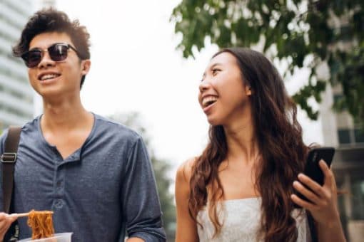 A smiling couple chats while walking down an urban sidewalk.