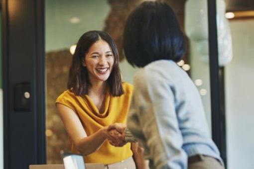 Woman in yellow shaking hands with a colleague in an office.