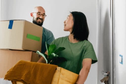  A man  and woman carry boxes and a plant moving items.