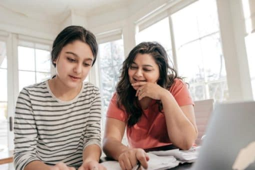 A mother and daughter work on a budget at the kitchen table.