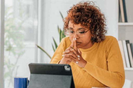 Woman in a yellow sweater focusing on a tablet at a desk.