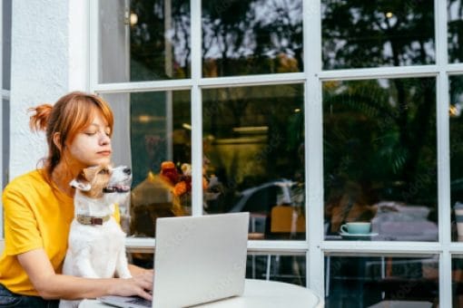 Woman sits outside with her dog in lap typing on her laptop