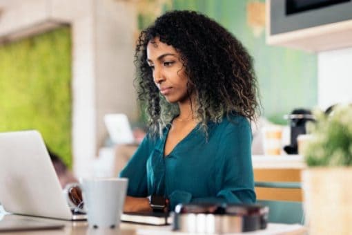 A woman works from her laptop in modern, bright, open office space.