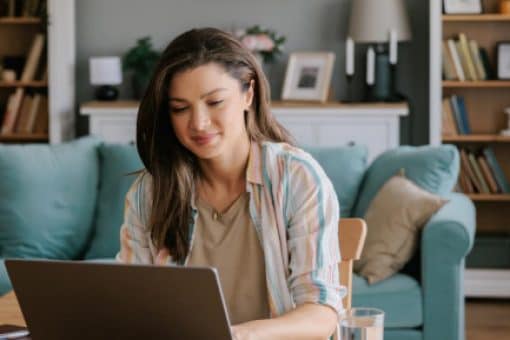 A woman sits at a desk in her living room and uses her laptop to pay her credit card bill.