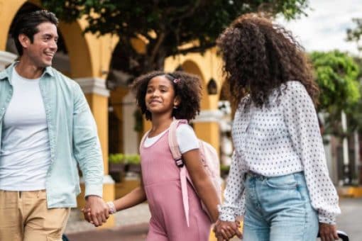 Mom, dad, and young daughter bring their luggage inside a hotel.