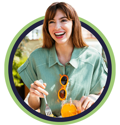 Woman in linen shirt smiling and eating breakfast on sunny patio