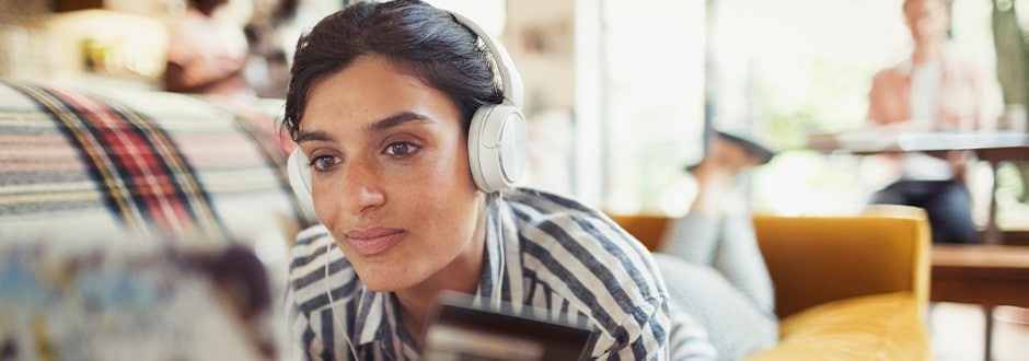 Woman on a sofa with headphones on and looking at her laptop