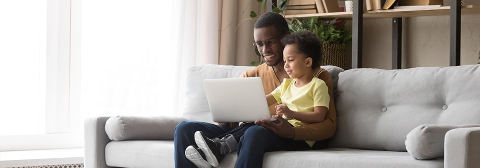 Young father with his son sitting on a sofa and using a laptop, calculating the costs and benefits of refinancing his home.