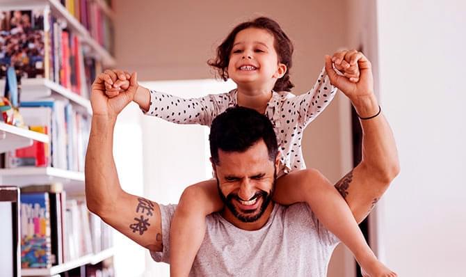 A man is holding a little girl on his shoulders in a living room.