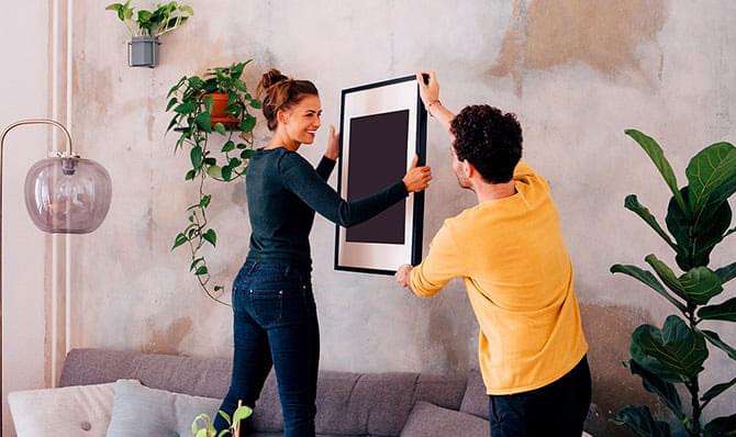 A man and woman hanging a picture frame in a living room.