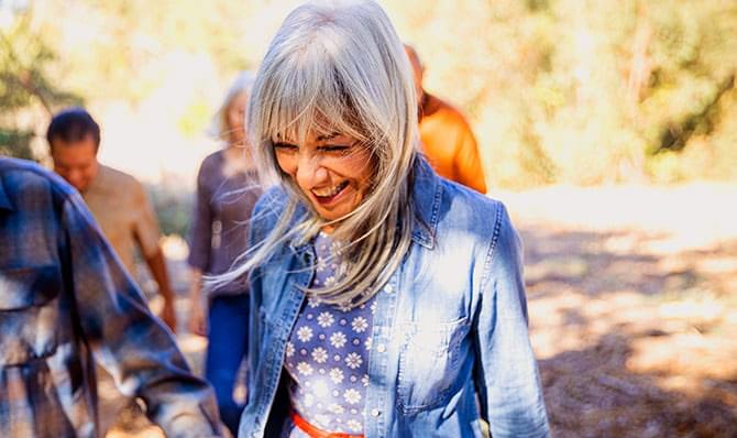 A retired woman smiling and walking through the woods with people.